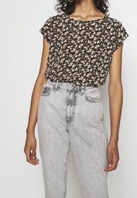 Blusa nera floreale con maniche corte a campana, decorata con piccoli fiori rosa e bianchi. Abbinata a jeans di denim grigi chiari a vita alta.