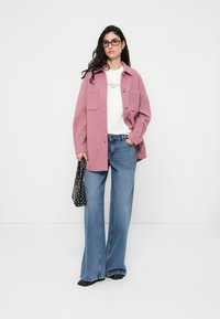 Ροζ φαρδιά μπουφάν με μεγάλες μπροστινές τσέπες, καφέ κουμπιά· συνδυασμένο με λευκό μπλουζάκι και μπλε τζιν με φαρδιά παντελόνια. Μαύρη τσάντα με πουά.