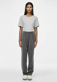 Graues T-Shirt mit kurzen Ärmeln, kombiniert mit hoch sitzenden, gefäßten grauen Hosen und weißen Turnschuhen mit beigen Akzenten.