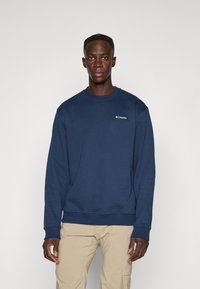 Marineblauwe sweatshirt met ribbelmanchetten en -zoom; heeft een klein logo op de linkerborst. Zachte stof en een klassieke ronde hals.