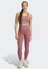 Athletikset in staubrosa, bestehend aus einem Cropped-Top mit breiten Trägern und hoch geschnittenen Leggings. Weiße Logo-Akzente auf beiden Teilen.