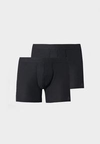 Deux boxers noirs côtelés, l'un devant l'autre, avec des ceintures élastiques et un logo subtil sur la partie inférieure de la jambe gauche.