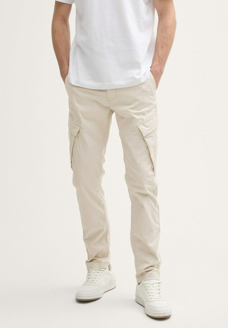 Beige Cargo-Hosen mit Seitentaschen, aus leichtem Stoff gefertigt. Kombiniert mit weißen Sneakers. Einfaches, gerades Design.