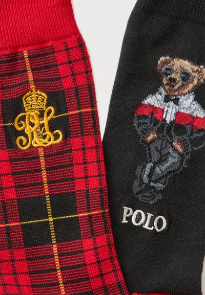 Deux chaussettes, l'une à carreaux rouge et noir avec une broderie de couronne dorée, l'autre noire avec un ours portant des lunettes de soleil et une veste, et le texte "POLO".