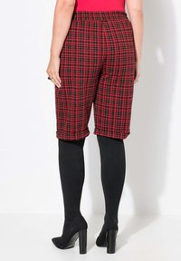 Rödrutig och svart culottebyxor med elastisk midja, kort längd och uppvikt nederkant, kombinerat med svarta täckande strumpbyxor och svarta högklackade skor.