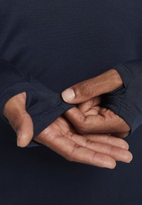Mains à la peau foncée ajustant le trou pour le pouce sur le poignet d'une chemise à manches longues bleu marine.