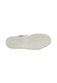 Svart sneaker med en vit gummisula, med ett texturerat greppmönster och en slät, rund tå. Mittensektionen har varumärkesdetaljer.