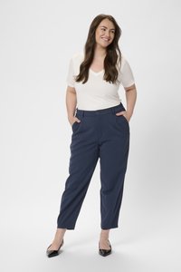 Pantalones de corte navy con bolsillos delanteros, textura suave y perneras ajustadas. Combinados con una blusa blanca de escote en V y mangas cortas, y tacones negros.
