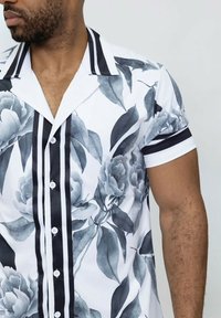 Chemise à manches courtes en tissu blanc, ornée d'un motif floral gris et de rayures verticales noires sur le col et la patte de boutonnage.