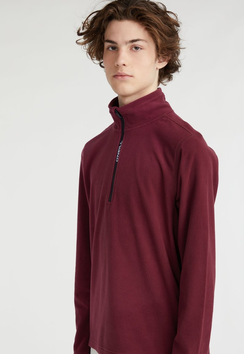 Pull en polaire bourgogne avec un col haut, zip quart et une fermeture éclair noire. Texture douce et manches longues, avec un logo sur la poitrine.