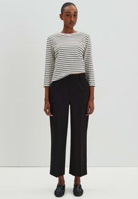 Maglietta a maniche lunghe a righe in bianco e nero abbinata a pantaloni neri a vita alta, con gamba dritta e design minimalista.