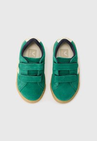 Sneakers verdes em camurça com duas tiras de Velcro, sola de borracha castanha e interior em azul-marinho. Apresenta um logo na lateral.