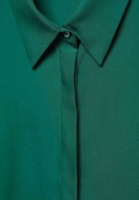 Chemise verte à col, avec une texture lisse, dotée d'une fermeture à boutons sur le plastron et d'une couleur unie sans motifs.