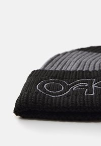 Black ribbed knit beanie featuring a folded brim; gray embroidered logo on the front, with a textured pattern throughout.
