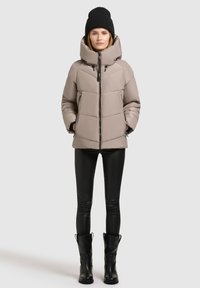 Beige puffjacka med hög krage, kviltat mönster och svarta detaljer. Matchad med svarta leggings och höga svarta stövlar.