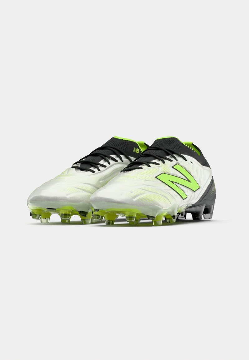 Un paio di scarpe da calcio New Balance bianche e verde neon con lacci neri e suola chiodata su sfondo bianco.
