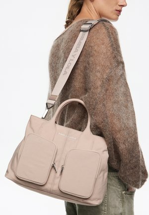 Bolso de mano beige hecho de material suave, con dos bolsillos frontales grandes, cierres de cremallera y dos asas en la parte superior. Correa ajustable con detalle del logo.