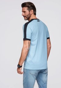 Světle modré tričko s krátkým rukávem, černými akcenty na ramenech a límcem. Bavlněná směs s hladkou texturou. Neformální střih a minimalistický design.