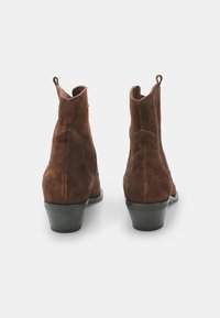 Botas ankle de ante marrón con un ligero tacón, que cuentan con tiradores en la parte posterior y una suela de goma negra lisa. Diseño limpio sin adornos.