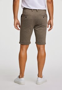 Bruine katoenen shorts in een blend met opgerolde omslagen, achterzakken met knopen en een gladde textuur. G gedragen met witte sneakers.