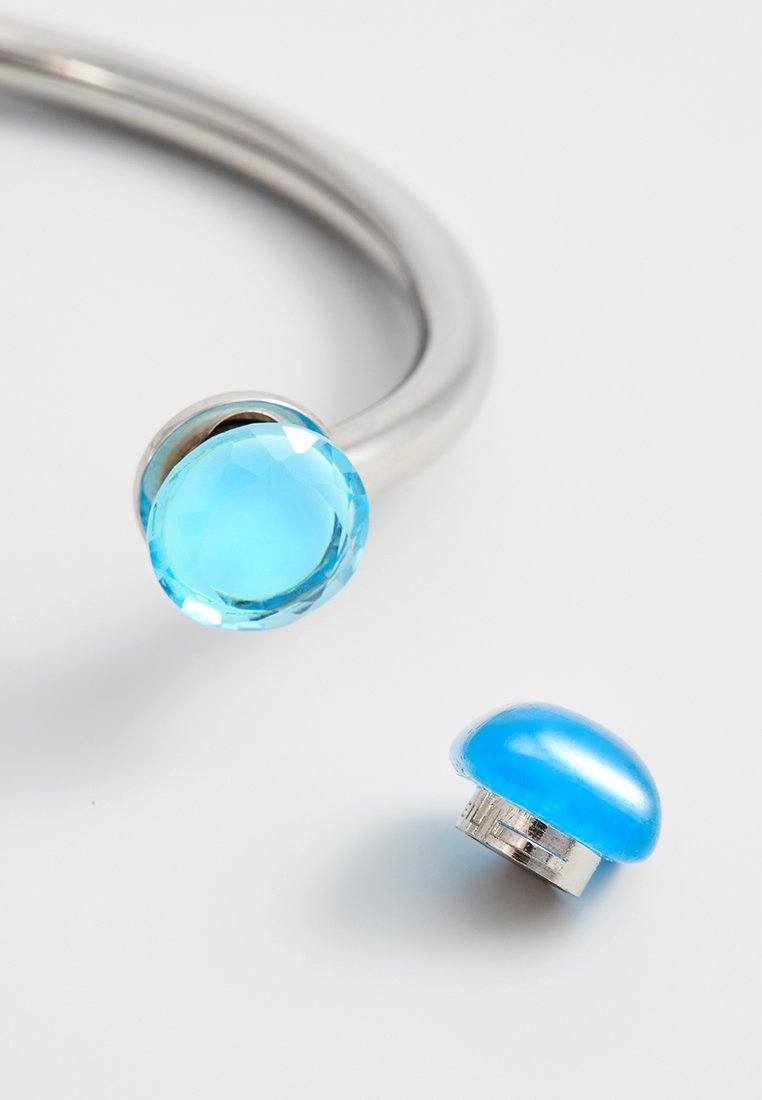 Zilveren armband met een grote, facette blauwe edelsteen en een verwijderbare, gladde blauwe accent. Beide hebben glanzend metalen hardware.