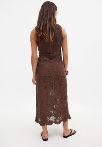 Maxi dress in crochet marrone con motivi floreali, corpetto aderente e schiena scoperta. Rifinito con bordi scallop.