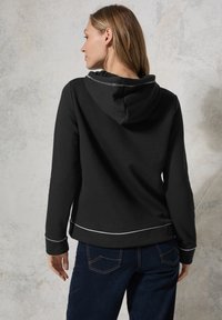Zwarte hoodie met witte stiksels. Heeft een relaxte pasvorm, lange mouwen en een kangoeroezak. Zachte stof.