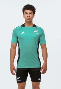 Turkos sporttröja med svarta accenter, korta ärmar och "All Blacks"-logotyp; parat med svarta shorts med vita ränder.