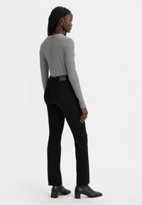 Jeans negros acampanados con cintura alta, combinados con una blusa de manga larga a rayas grises y blancas. Presentan bolsillos laterales y un acabado texturizado.