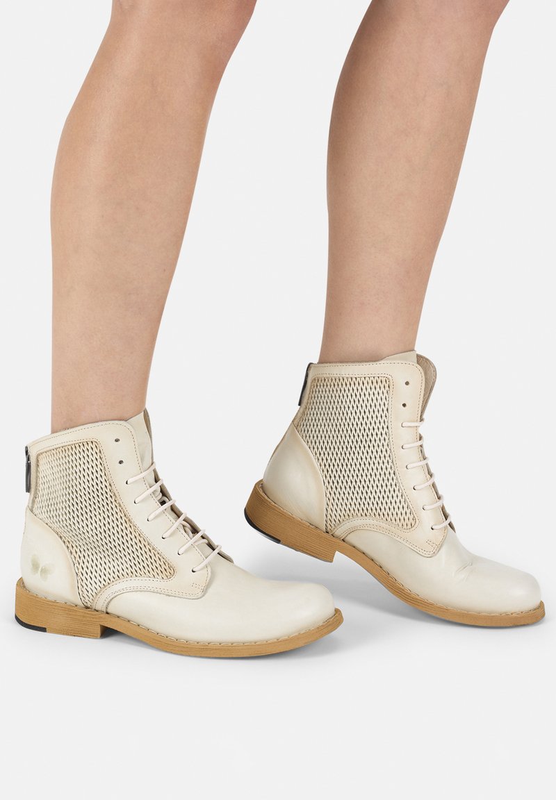 Botines de cuero crema con cordones, panel lateral de malla, suela plana color tostado y costuras reforzadas, que cuentan con una cremallera en la parte posterior.