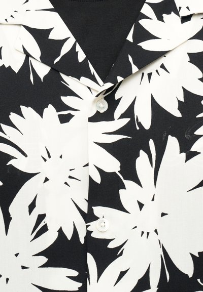 Chemise à motif floral en noir et blanc, avec col et deux boutons blancs visibles sur un fond de sous-vêtement noir.