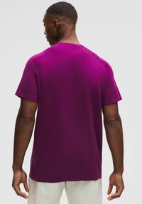 Kortærmet T-shirt i strålende lilla, med et tekstureret stof, rund halsudskæring og raglanærmer. Diskret branding nær kanten.