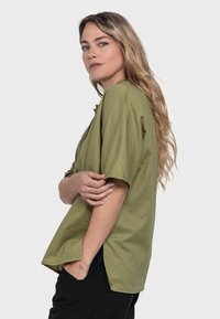 Olive green shirt with a relaxed fit, short sleeves, and side slits. Made from soft fabric, features a clean neckline and minimal detailing.