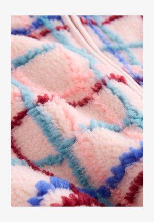 Manta de forro polar con base rosa, que presenta un patrón de diamantes en azul claro, rojo y acentos azul oscuro; textura suave y aterciopelada.