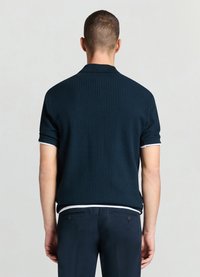 Polo à manches courtes côtelé bleu marine avec un bord de col blanc, offrant une coupe décontractée et un tissu texturé. La vue de dos montre des détails discrets du design.