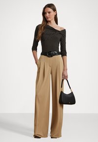 Svart polka dot bodysuit med off-shoulder design, kombinert med beige vide bukser og en svart veske med gull detaljer.