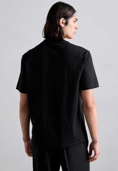 T-shirt en coton noir à manches courtes, col rond et coupe décontractée. Texture lisse et design minimaliste, sans motifs ou accents visibles.