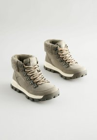 Szare buty trekkingowe z beżowym futrzanym kołnierzem, metalowymi oczkami i teksturowanymi podeszwami. Plecione sznurówki dodają detali. Odpowiednie do użytku na zewnątrz.