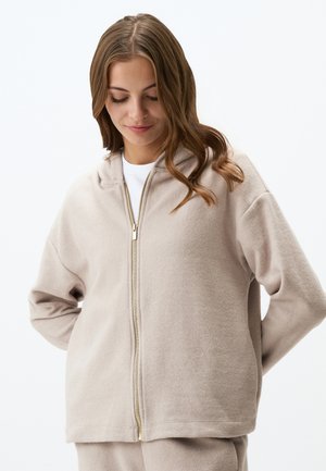 Felpa beige con zip realizzata in morbido pile. Caratterizzata da un cappuccio con coulisse, maniche lunghe e una vestibilità rilassata. La cerniera dorata aggiunge un tocco di dettaglio.