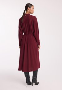 Bordowa midi sukienka z długimi rękawami i wiązanym w pasie, z/details at the back and a flowy silhouette. Połączona z czarnymi kozakami do kolan.