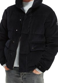 Giacca puffer in corduroy blu navy con colletto alto, zip frontale, chiusure a scatto e due tasche laterali con polsini a coste.