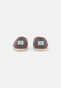 Brune kanvas slip-on sko med et mykt stoffdesign, som har en lysfarget gummisåle og lyseblå etiketter på hælen.