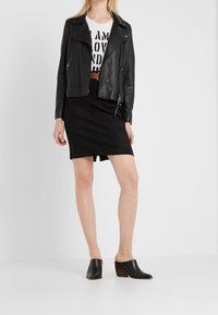 Svart läderbikerjacka över en vit grafisk t-shirt, matchad med en svart figurnära kjol och svarta öppen-tå stövletter med klack.