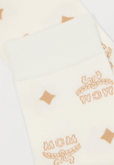 Kremaste čarape s rebrastim rukavom, koje sadrže ponavljajući svijetlosmeđi logo i uzorak dijamanata kroz cijelu površinu. Mekana tekstura tkanine.