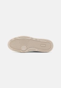 Sneaker sole in beige rubber featuring textured grip patterns, circular and zigzag designs, and a central circular accent.
