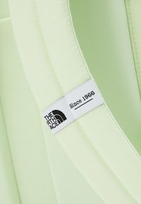 Sangle de sac à dos vert clair avec une étiquette en tissu blanche affichant le logo "The North Face" et le texte "Since 1966" en noir.