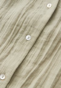 Light beige textured fabric with vertical wrinkles and four white buttons sewn in a vertical line.