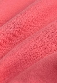 Korálová pletenina s jemnou textúrou, so zlátaným tkaním a subtílnymi farebnými variáciami na povrchu, vytvárajúcimi hĺbku a dimenziu.