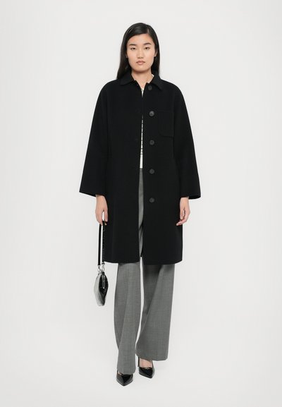 Black wool coat with a collared neckline, front pocket, and six buttons. Paired with gray wide-leg trousers and pointed black heels.