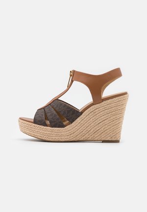 Kilehæle sandal med flettet juteplatform, brun læderankelrem og mørke teksturerede stropper, med forrest lynlås lukning.